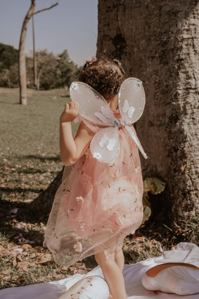 Little girl in a pink dress and butterfly wings playing outside by a tree